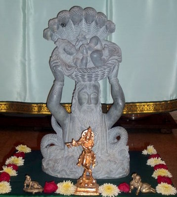 A statue depicting Vasudeva carrying new born lord Krishna through river Yamuna in a rainy night with SheshNag giving a canopy cover to the new born